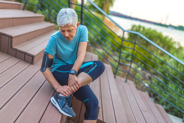 Senior Woman in pain while running in park, knee injury. Senior woman with an expression of severe...