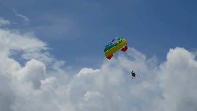 4K. excited tourists hanging on parasailing flying high in the sky, outdoor extreme sport summer activity. colorful parachute on blue sky background
