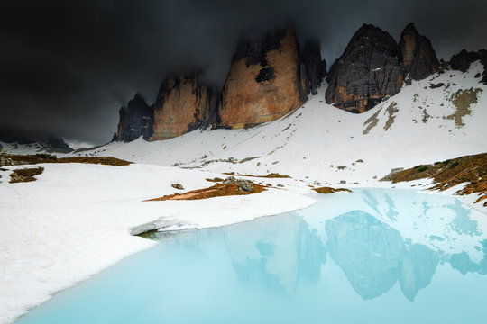 Les Tre Cime di Lavaredo, sommet des Alpes, à 2 999 m d'altitude sous les nuages avec un lac au premier plan