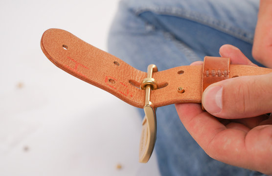 man makes by hands leather belt with buckle. handmade hobby. young man resting by manufacture his designer belts. man with a screwdriver in his hands twists rivets close up on white studio background.