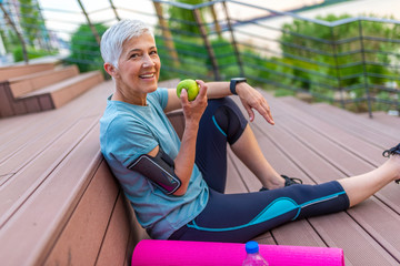 Sporty woman eating apple. Beautiful woman with gray hair in the early sixties relaxing after sport...