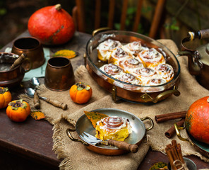 Autumn outdoor still life with pumpkin cinnamon buns in oval glass dish on wooden table