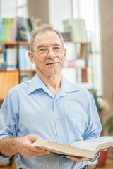 Smiling senior man with open book in the library