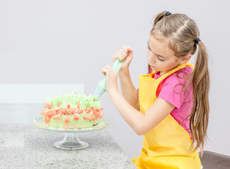 Little girl decorating cake in the kitchen at home
