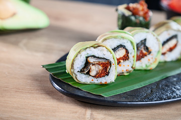 Close up view on set of sushi roll. California roll with salmon, avocado and caviar served on wooden table. Japanese cuisine. Copy space. Served sushi for menu. Healthy food, seafood