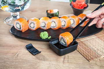 Close up view on hand holding chopsticks and dunk sushi in soy sauce. California roll with salmon. Japanese cuisine. Copy space. Served sushi for menu. Healthy food, seafood
