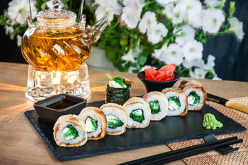 Close up view on set of sushi roll. California roll with eel, avocado and caviar served on black stone on wooden table. Japanese cuisine. Copy space. Served sushi for menu. Healthy food, seafood