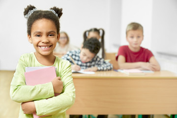 Happy schoolchild standing in classroom, holding books.