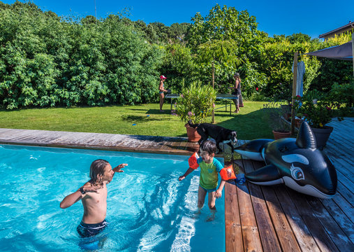 Two boys of 5 years old and 13 years old playing in the swimming pool, in the background a mother playing ping pong with her daughter