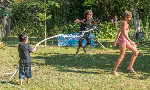 Two boys of 4 years old and 12 years old and a ten-year-old girl playing with a hose in the garden