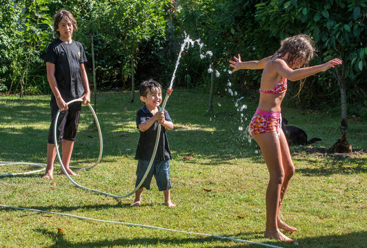 Two boys of 4 years old and 12 years old and a ten-year-old girl playing with a hose in the garden