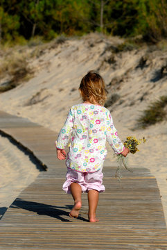 Two-year-old girl walking on duckboards at the beach, holding a bunch of flower