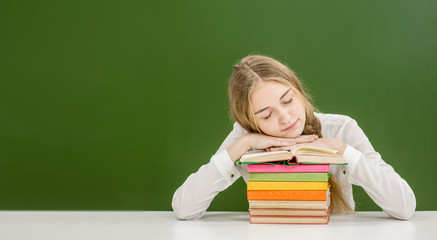 Teen girl sleeping on books in classroom. Empty space for text