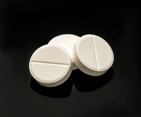 White pills on a black background. Macro