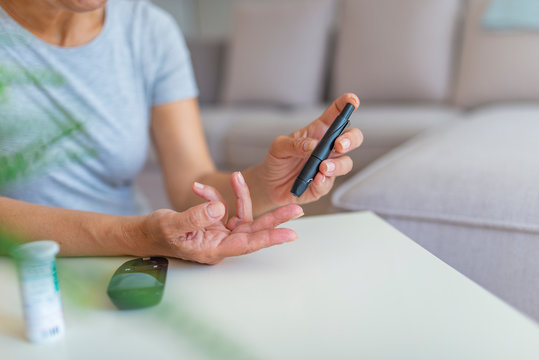 Woman using lancelet on finger. Diabetes doing blood glucose measurement. Woman using lancet and glucometer. Diabetes checking blood sugar level. Woman using lancelet and glucometer at home.