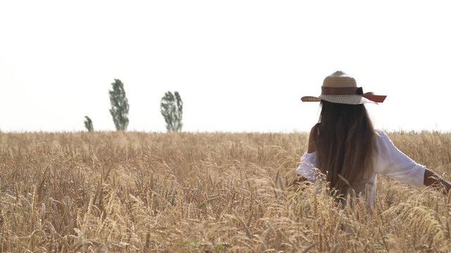 An attractive woman wearing straw hat walking in the field on daylight. Cheerful girl enjoying her time