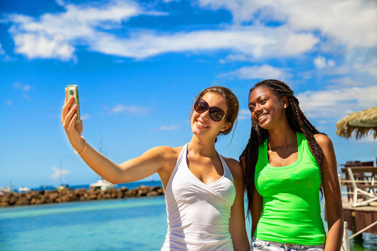 2 smiling girls taking a selfie against blue sky background.