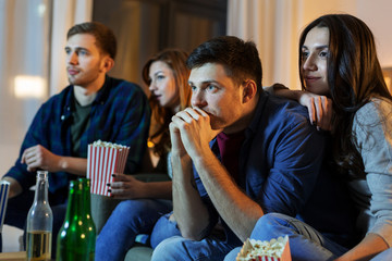 friendship and leisure concept - friends with beer and popcorn watching tv at home at night