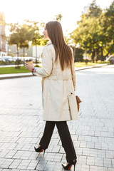 Fototapeta premium Photo from back of brunette caucasian woman drinking takeaway coffee while walking on city street
