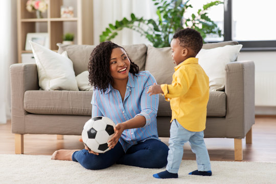 Childhood, Kids And People Concept - Happy African American Mother And Her Baby Son Playing With Soccer Ball Together On Sofa At Home