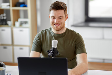 technology, mass media and podcast concept - happy young male audio blogger with laptop computer...