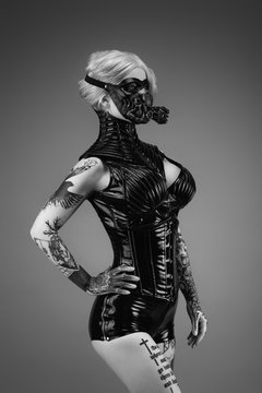 Portrait of a tattooed young woman wearing latex clothes and a gas mask