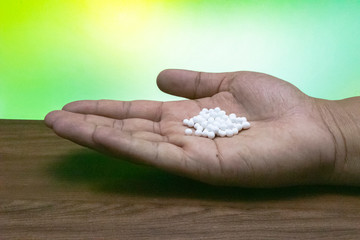 Close-up image of homeopathic pills in man's hand on wooden table with green mix yellow background