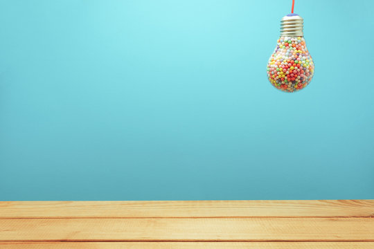 Creative lightbulb filled with multi colored ball on a BLUE background behind and red wooden floor or table down. Best idea concept.