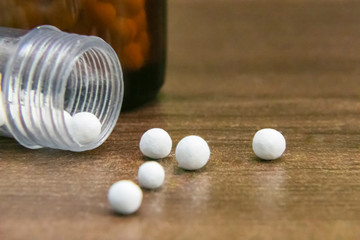 Homeopathic medicine bottle consisting of white pills scattered on wooden surface