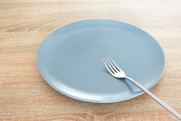 Empty gray plate and silver fork on wooden table