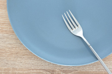 Close-up empty gray plate and silver fork on wooden table