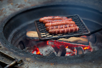 Forest Dinner tourist on grill. Delicious sausages are fried on fire in evening in the forest. dying embers of meat dinner traveler in forest