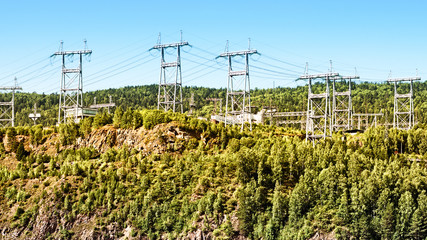power electricity lines high tower on rocky cliff side wide view of electric line in forest mountains landscape energy transmission distribution equipment in natural environment