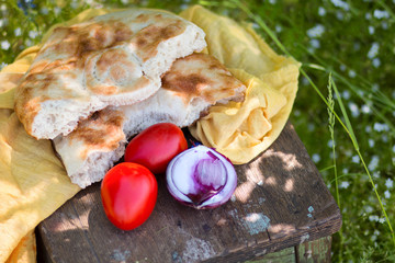 Country food in style of the farmer: the baked bread, onions, tomatoes on an old wooden stool outdoors in sunny summer day