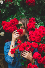 young woman near the bush of red roses in a garden