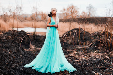 A girl of Asian appearance stands near the lake on the ashes in a blue dress with white hair on her shoulder sits a dragon