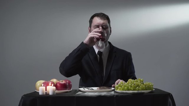 Portrait of a confident bearded man in a business suit sitting at a table and drinking red wine from a wine glass.