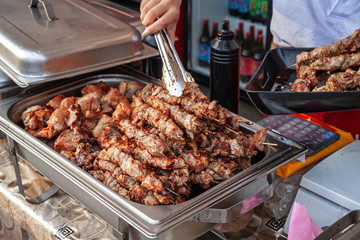 Cook puts shish kebab in a dish on the street fast food display.