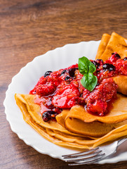 Pancakes with fresh berries jam in white plate on wooden background