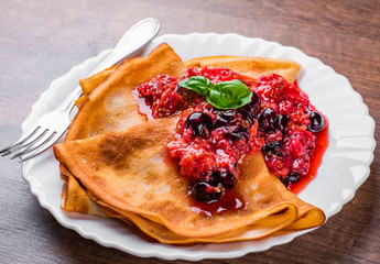 Pancakes with fresh berries jam in white plate on wooden background