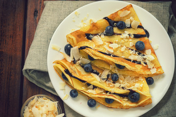 Homemade crepes with blueberries, coconut flakes and chocolate sauce