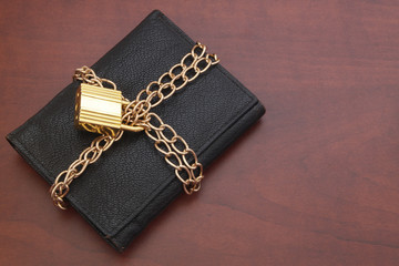 Fototapeta premium Locked wallet with chain and golden padlock on wooden table with room for texr. Finance safety concept