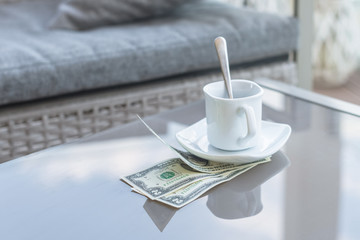 American dollars bill and empty cup of coffee on a glass table of outdoor cafe. Payment, tip.