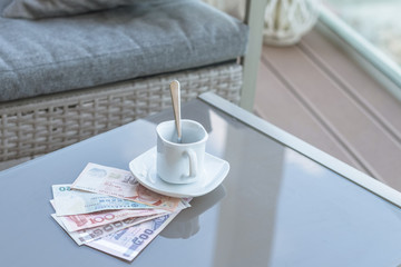 Hong Kong, Indonesia, Malaysia, Thai, Singapore dollar and empty cup of coffee on a glass table of outdoor cafe. Payment, tip.