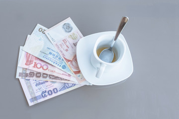 Hong Kong, Indonesia, Malaysia, Thai, Singapore dollar and empty cup of coffee on a glass table of outdoor cafe. Payment, tip.