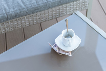 Thai money and empty cup of coffee on a glass table of outdoor cafe. Payment, tip.