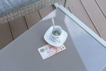 Singapore ten dollars bill and empty cup of coffee on a glass table of outdoor cafe. Payment, tip.