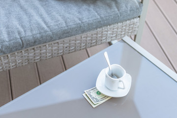 American one dollar bill and empty cup of coffee on a glass table of outdoor cafe. Payment, tip.