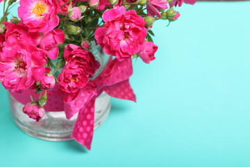 Bouquet of crimson roses in a glass vase with a bow. It stands on the surface of mint color.
