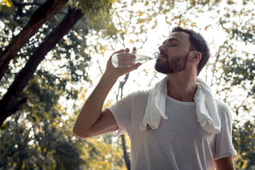 Handsome man drinking water after exhausting exercise.